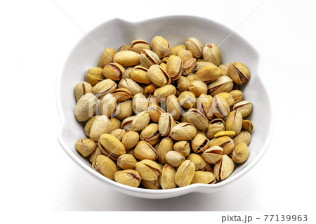 A white bowl with a bunch of salted and roasted pistachio seeds on a white background. Perfect shot for vegan diet,. A white bowl with a bunch of salted and roasted pistachio seeds on a white background. Perfect shot for vegan diet,. 77139963