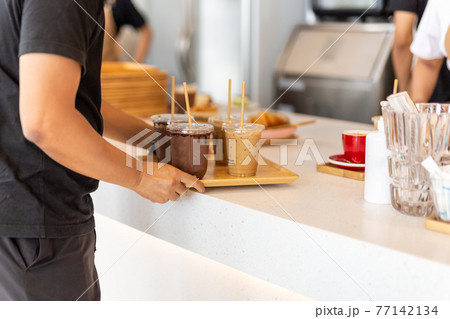Waiter serving iced coffee and iced chocolate on wooden tray to customer. 77142134