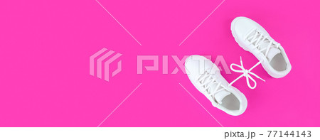 Pair of white sport shoes connected with laces bow on pink background. Simple flat lay with copy space. Pair of white sport shoes connected with laces bow on pink background. Simple flat lay with copy space. 77144143