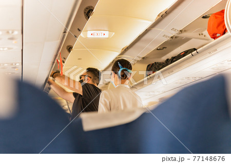 Flight atttendant attendant helping passenger to put luggage cabin compartment. 77148676