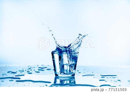 Ice that fell into the glass with water splashing from glass isolated on blue background Ice that fell into the glass with water splashing from glass isolated on blue background 77151503