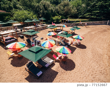 Sun loungers under colored umbrellas on the beach against the backdrop of green mountains 77152667