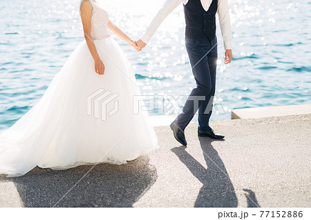 The bride and groom are walking hand in hand on the road by the sea, close-up 77152886