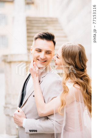 Bride holds her palm on the chin of smiling groom against the background of the steps of an ancient building in Bergamo 77153116