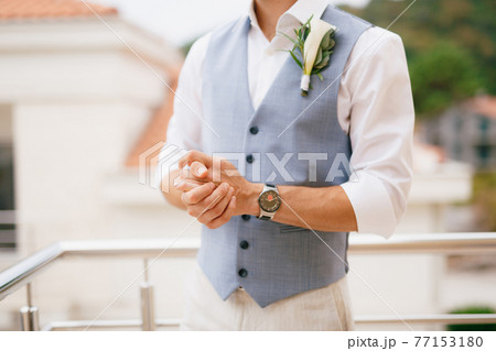 The groom in a shirt and vest with a boutonniere stands on the balcony in the morning before the wedding ceremony 77153180