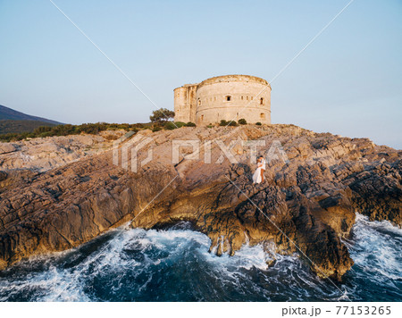 The bride and groom are embracing on the rocky seashore near the ancient fortress Arza  77153265