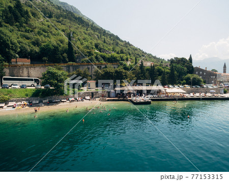 Aerial view of the beach of Perast city with various buildings and green mountains in the background Aerial view of the beach of Perast city with various buildings and green mountains in the background 77153315