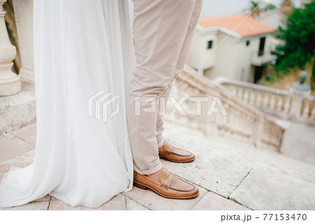 Legs of the bride and groom hugging on the beautiful ancient stairs of the temple in Prcanj, close-up Legs of the bride and groom hugging on the beautiful ancient stairs of the temple in Prcanj, close-up 77153470