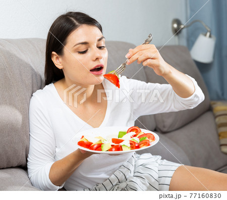 Woman eating salad on sofa 77160830