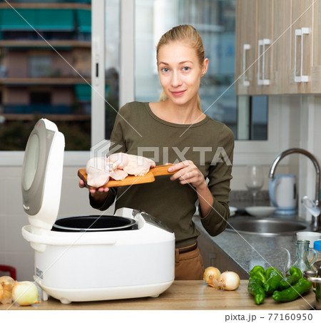 Smiling woman cooking with electric multicooker at home kitchen 77160950