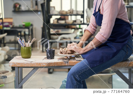 Handmade. Cropped shot of mature woman in apron shaping, creating clay ceramics in pottery workshop studio Handmade. Cropped shot of mature woman in apron shaping, creating clay ceramics in pottery workshop studio 77164760