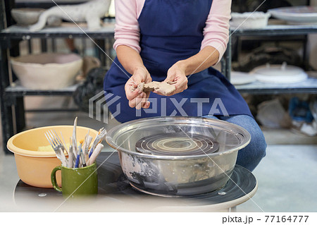 Cropped shot of woman in blue apron creating handmade clay ceramics in pottery workshop studio Cropped shot of woman in blue apron creating handmade clay ceramics in pottery workshop studio 77164777