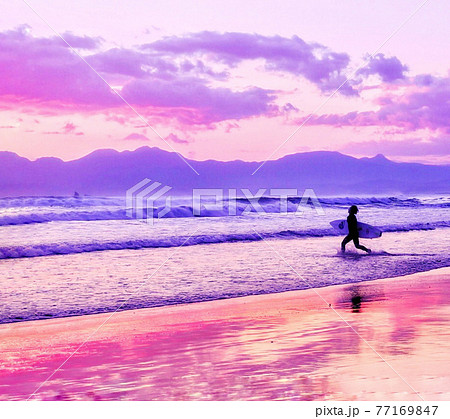 ピンクの夕焼けの海でサーフィンをする人の写真素材