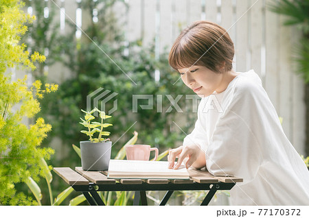 テラスでコーヒーを飲みながら読書する若い女性 77170372