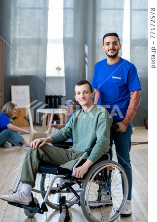 Young male volunteer standing next to guy in a wheelchair 77172578