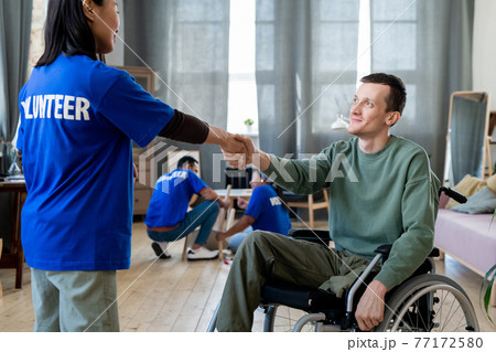 A young female volunteer shaking hands with a man in a wheelchair A young female volunteer shaking hands with a man in a wheelchair 77172580
