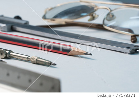 Glasses and drawing supplies are on the table in the school classroom. University academic subjects for geometry.Ruler, compass, pencil, caliper and glasses on a white background. 77173271