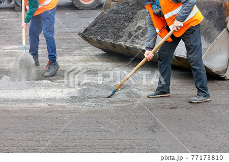 Road workers shovel old crushed asphalt off the roadway and load it into the grader bucket. Road workers shovel old crushed asphalt off the roadway and load it into the grader bucket. 77173810