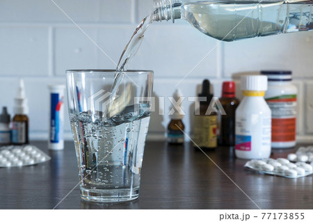 Pour water into a glass against the background of pills and medications. Clean water, liquid streams. Water from the bottle is poured into a glass. 77173855