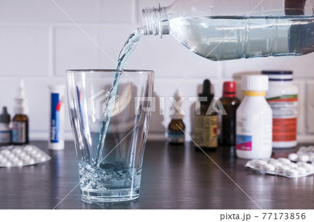 Pour water into a glass against the background of pills and medications. Clean water, liquid streams. Water from the bottle is poured into a glass. 77173856