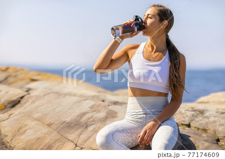 Female Athlete Drinking Water During Outdoor Workout by the Sea Female Athlete Drinking Water During Outdoor Workout by the Sea 77174609