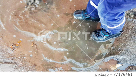 Close-up of a child's feet in rubber boots, a boy child happily playing with a shovel in a muddy puddle with snow and ice, in the early spring in the yard 77176461