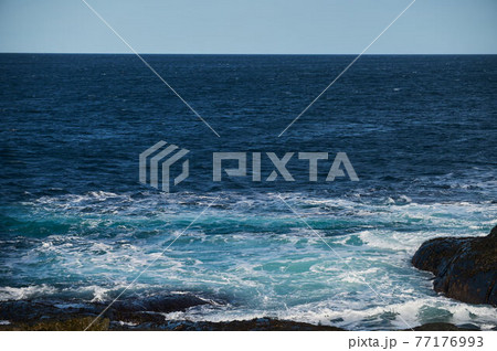 Small sea waves break against the stones of the shore. A bright sunny day and white foam of the waves. Melting glaciers as an environmental impact of air pollution. Small sea waves break against the stones of the shore. A bright sunny day and white foam of the waves. Melting glaciers as an environmental impact of air pollution. 77176993