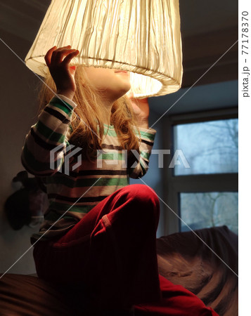 Kid in shade, happy pretty little girl plays with lampshade like hat 77178370
