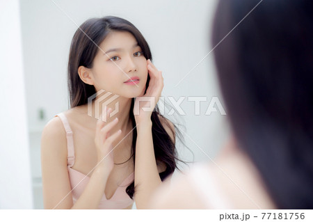 Beautiful young asian woman smiling look at mirror of checking face with skin care and cosmetic. 77181756