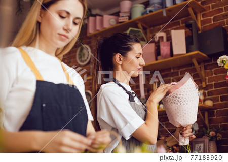 Woman florist together with assistant collect bouquets in flower shop. Woman florist together with assistant collect bouquets in flower shop. 77183920