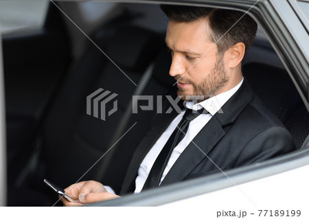 Wealthy manager sitting in car and using smartphone 77189199