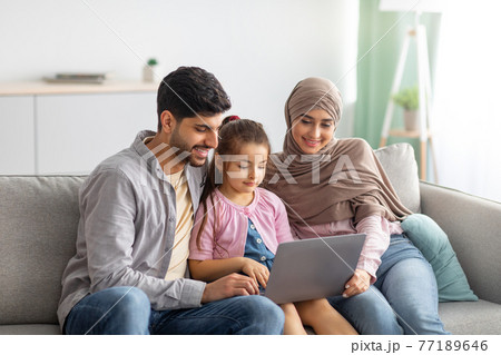 Young muslim parents and girl using laptop together, surfing internet or having video chat with someone, sittig on sofa Young muslim parents and girl using laptop together, surfing internet or having video chat with someone, sittig on sofa 77189646