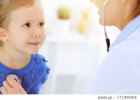 Doctor examining a little girl by stethoscope. Happy smiling child patient at usual medical inspection. Medicine and healthcare concepts 77190069