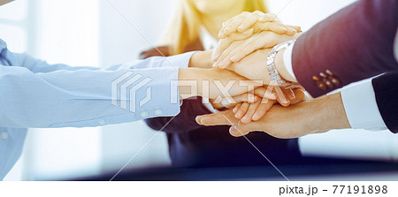 Business team showing unity with their hands together in sunny office. Group of people joining hands and representing concept of friendship and teamwork 77191898