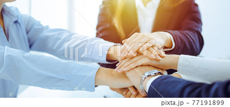 Business team showing unity with their hands together in sunny office. Group of people joining hands and representing concept of friendship and teamwork 77191899