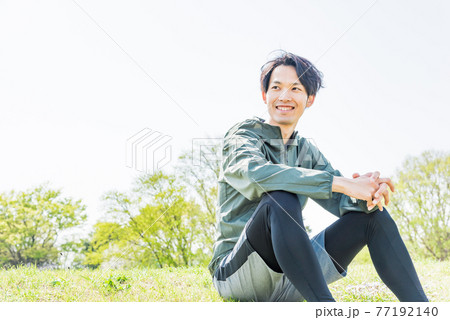 ランニング中に公園で休憩をする若い男性 77192140