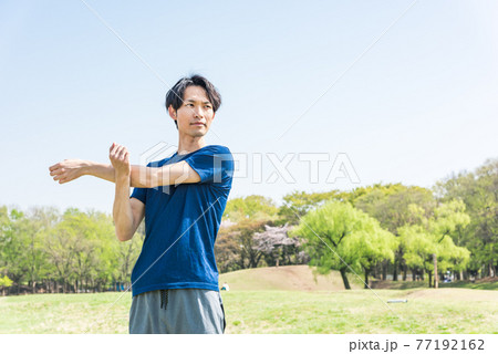 公園でランニング前にストレッチをする若い男性 77192162