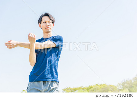 公園でランニング前にストレッチをする若い男性 77192180