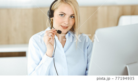 Blonde business woman sitting and communicated by headset in call center office. Concept of telesales business or home office occupation Blonde business woman sitting and communicated by headset in call center office. Concept of telesales business or home office occupation 77194935