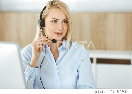 Blonde business woman sitting and communicated by headset in call center office. Concept of telesales business or home office occupation 77194936