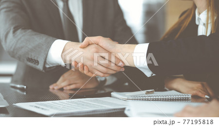 Unknown businessman shaking hands with his colleague or partner above the glass desk in modern office, close-up. Business people group at meeting 77195818