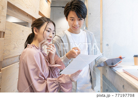 コワーキングスペースで立って書類を見ながら会話をする笑顔の若い男女 コワーキングスペースで立って書類を見ながら会話をする笑顔の若い男女 77197708