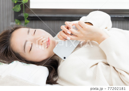 ベッドに寝転がってスマホを持つ女性 77202181