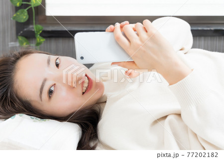 ベッドに寝転がってスマホを持つ女性 77202182