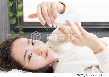 ベッドに寝転がってスマホを持つ女性 77202183
