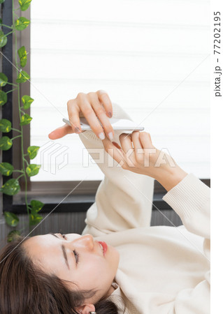 ベッドに寝転がってスマホを持つ女性 77202195