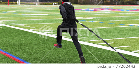 Runner pulling a sled with weights on a green turf field Runner pulling a sled with weights on a green turf field 77202442