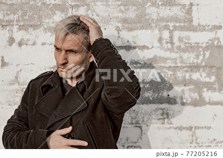 Middle aged blonde man in trendy clothes is posing in front of a white brick wall. Male fashion photoshoot. Men's mental health. Emotions. Front view, copy space. Middle aged blonde man in trendy clothes is posing in front of a white brick wall. Male fashion photoshoot. Men's mental health. Emotions. Front view, copy space. 77205216