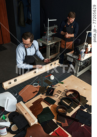 leather craftsmen working making measupenets in patterns at table in workshop studio 77205629