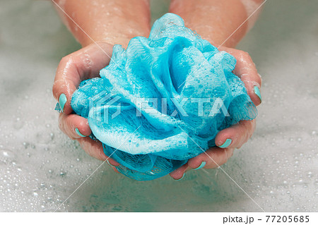 female hands holding a round soft synthetic washcloth in bath with water. Hands close-up. Spa treatment, body care, water background 77205685